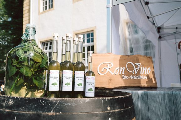Weinfass auf der viele Flaschen mit Pfefferminzlikör stehen. Ein Holzschild mit der Aufschrift Ron Vino Bio Weinliköre
