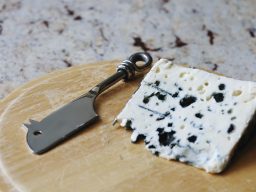 Holzbrett auf dem ein Hackbeil liegt und ein schönes großes Stück Käse mit Blauschimmel